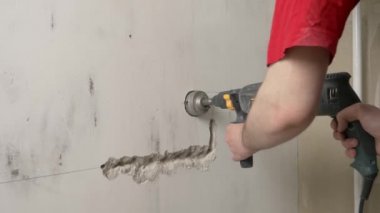 İnşaatçı bir duvar kazıyor, inşaat giysileri ve başlık takıyor, duvarları, inşaat konseptini, elektrik döşemesini delecek.