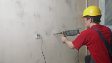 İnşaatçı bir duvar kazıyor, inşaat giysileri ve başlık takıyor, duvarları, inşaat konseptini, elektrik döşemesini delecek.
