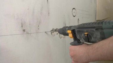 İnşaatçı bir duvar kazıyor, inşaat giysileri ve başlık takıyor, duvarları, inşaat konseptini, elektrik döşemesini delecek.