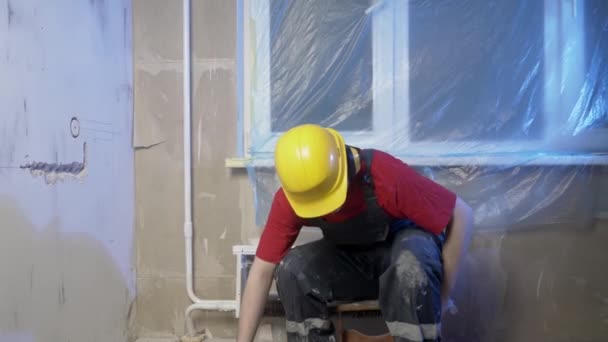 建筑工人坐下来休息 因为他工作太累了 他穿着建筑用的衣服 头戴安全帽 他会钻墙 思考建筑的概念 — 图库视频影像