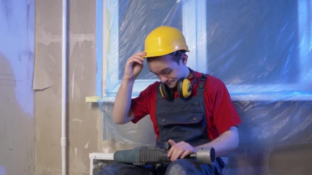 建筑工人坐下来休息 吃午饭 他穿着建筑服装 戴着头盔 他将钻墙 建筑的概念 铺设电力 — 图库视频影像