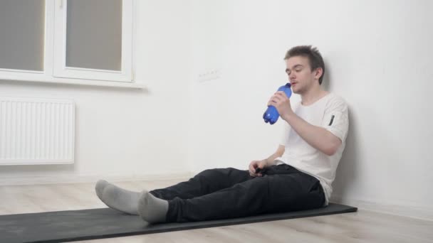 トレーニング中に青いボトルから水を飲む若いスポーツマン 彼は疲れている 隔離されながら自宅での訓練の概念 — ストック動画