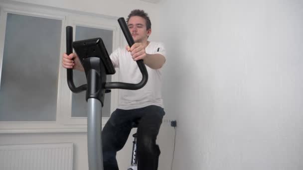 Evde Spor Yapan Yakışıklı Genç Adam Sabit Bir Bisiklette Oturuyor — Stok video