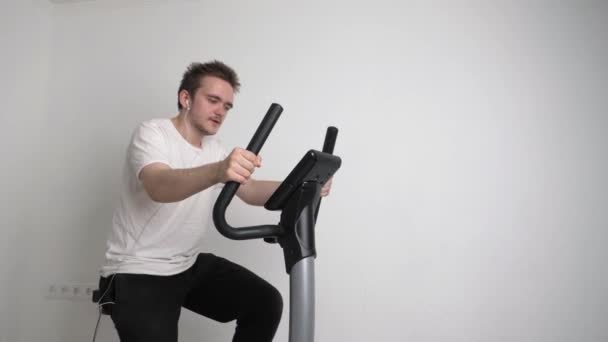 若いスポーティハンサムな男は自宅でスポーツをして 彼は静止自転車に座っている 自宅で演習を行うの概念 — ストック動画