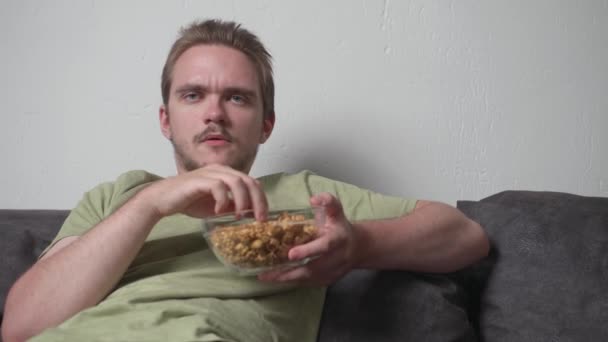 Ένας Νεαρός Κάθεται Στον Καναπέ Τρώγοντας Ποπ Κορν Και Πίνοντας — Αρχείο Βίντεο