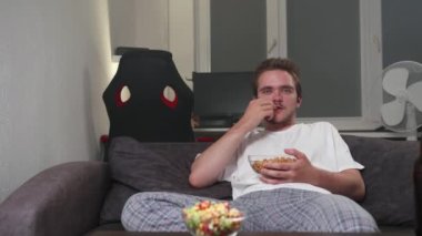 Genç yakışıklı sakallı adam televizyon izliyor. Genç bir adam oturma odasında dinleniyor ve eğlence, eğlence, video oyunları, televizyon konsepti olan bir video izliyor. Patlamış mısır ve bira