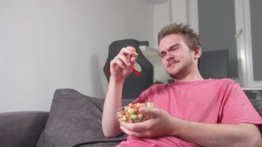 Genç yakışıklı sakallı adam televizyon izliyor. Genç bir adam oturma odasında dinleniyor ve eğlence, eğlence, video oyunları, televizyon konsepti olan bir video izliyor. Patlamış mısır ve bira