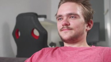 Genç yakışıklı sakallı adam televizyon izliyor. Adamın yüzü yakın, duyguları var. Eğlence, eğlence, video oyunları, televizyon konsepti. Patlamış mısır ve bira