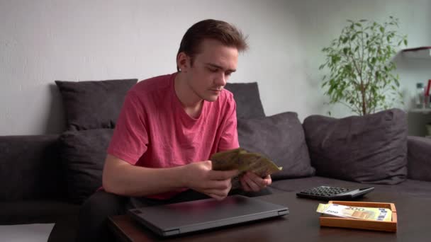 Joven Sentado Sofá Junto Mesa Con Ordenador Portátil Contando Dinero — Vídeos de Stock