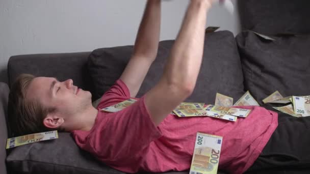 Genç Beyaz Bir Adam Kanepeye Uzanmış Etrafa Para Saçmış Zenginleştirme — Stok video