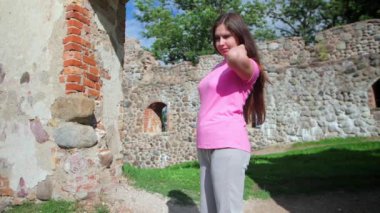 Pembe tişörtlü ve gri pantolonlu genç otantik bir kadın, Letonya 'nın manzarası olan Dobele Kalesi' nin kalıntılarına karşı poz veriyor.