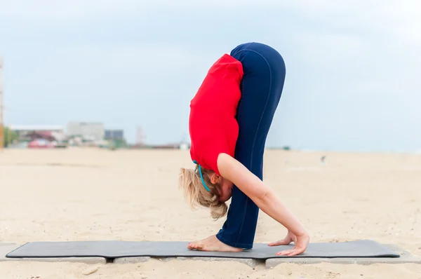 Sporty girl doing Supported Headstand, yoga asana Uttanasana on coast background — Stock Photo, Image
