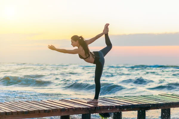 Woman practicing Warrior yoga pose outdoors over sunset sky background — Stock Photo, Image