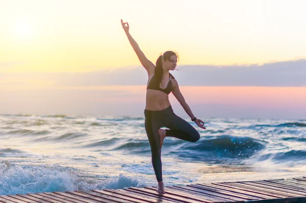 Young healthy woman practicing yoga on the beach at dawn. Sport and Healthy concept — Stock fotografie