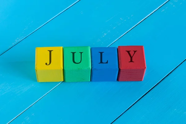 Assine julho na cor cubos de brinquedo infantil no fundo de madeira azul — Fotografia de Stock