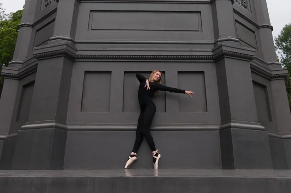 Bailarina na ponta dos pés en pointe perto da parede preta — Fotografia de Stock