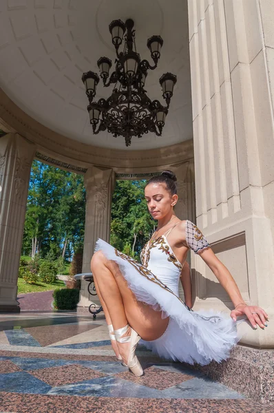 Ballerina sits near column, standing in pointe position. Outdoors, spring — Stock Photo, Image