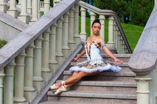 Ballerina senta-se nas escadas, de pé na posição de ponta. Ao ar livre, primavera — Fotografia de Stock