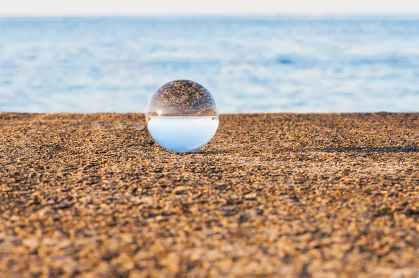 Sfera trasparente in vetro su fondo marino e superficie granulosa. Acqua. — Foto Stock