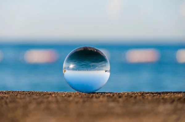 Bola transparente de vidrio sobre fondo marino y superficie granulada. Agua. —  Fotos de Stock