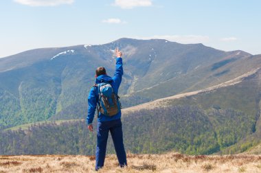 Mountaineer reaches the top of a mountain in sunny spring day.