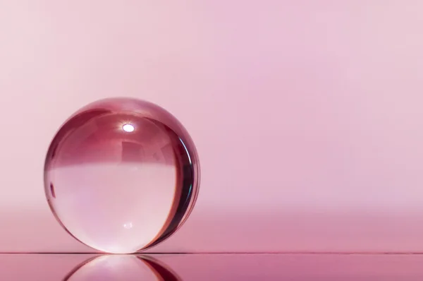 Bola transparente de vidrio sobre fondo rosa claro y superficie del espejo . — Foto de Stock