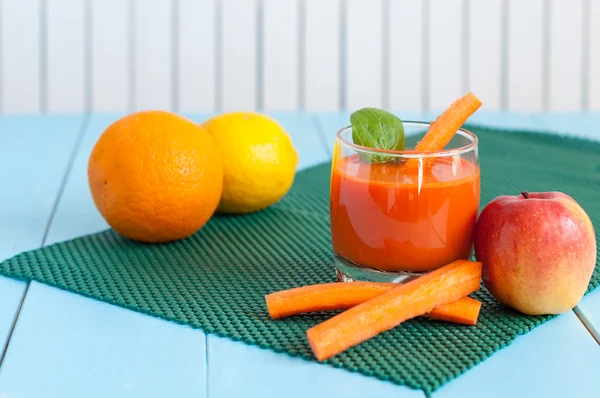 Jugo de zanahoria casero saludable en vidrio y zanahoria fresca, manzana, naranja, limón sobre fondo de madera clara . —  Fotos de Stock