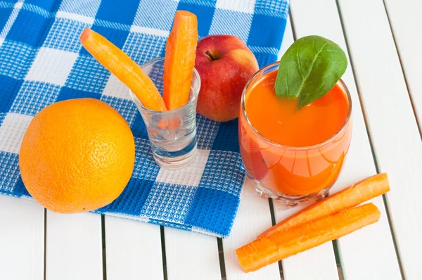 Здоровый домашний морковный сок в стакане и свежая морковь, яблоко, апельсин, шпинат на светлом деревянном фоне . — стоковое фото