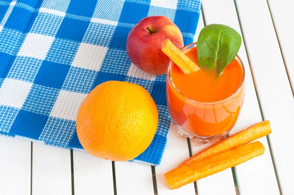 Здоровый домашний морковный сок в стакане и свежая морковь, яблоко, апельсин, шпинат на светлом деревянном фоне . — стоковое фото