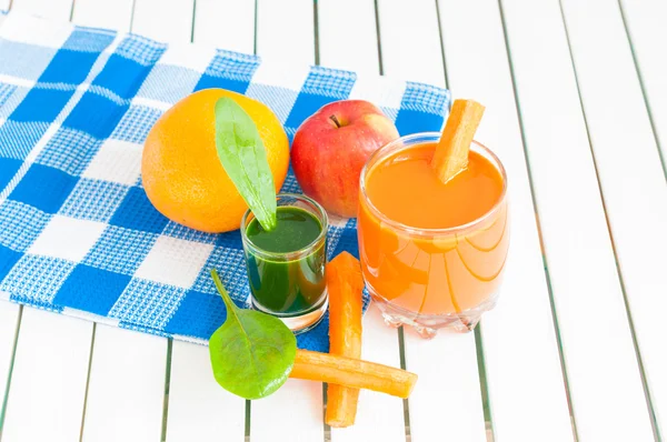 Здоровый домашний морковный сок в стакане и свежая морковь, яблоко, апельсин, лимон, шпинат на светлом деревянном фоне . — стоковое фото