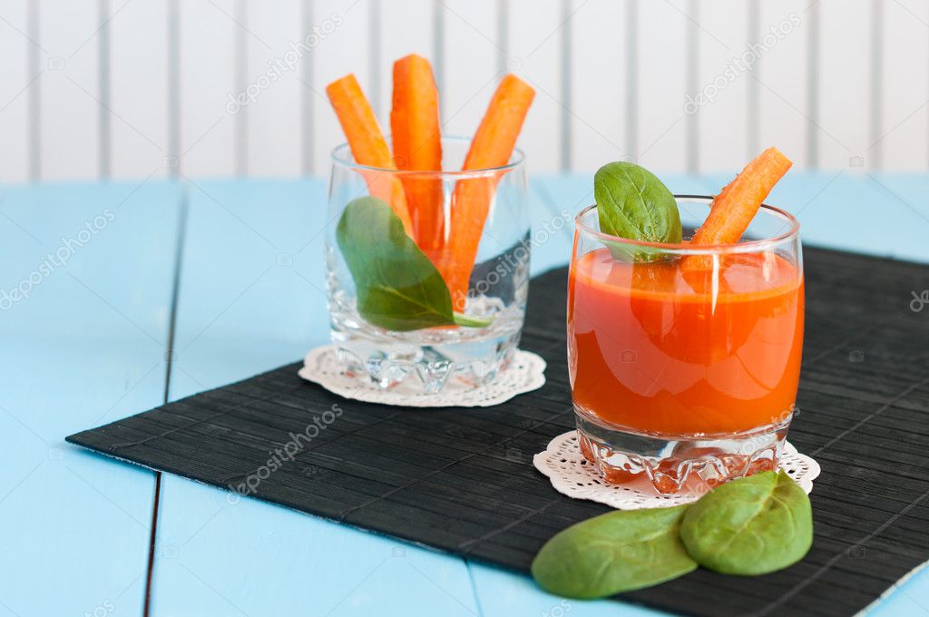 Healthy homemade carrot juice in glass and fresh carrots on light wooden background.