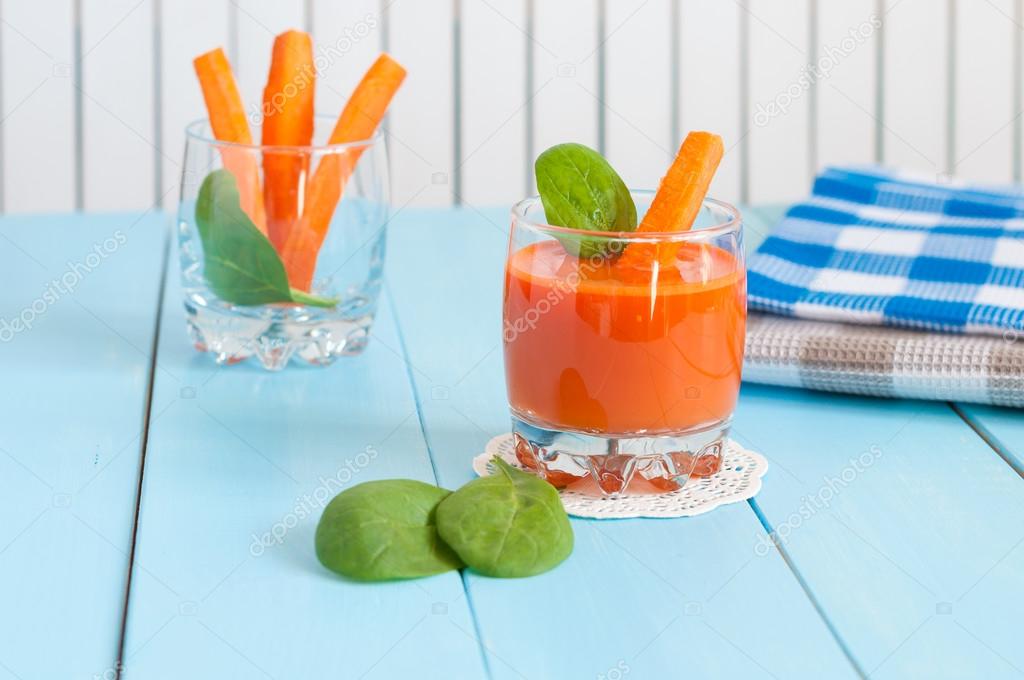 Healthy homemade carrot juice in glass and fresh carrots on light wooden background.