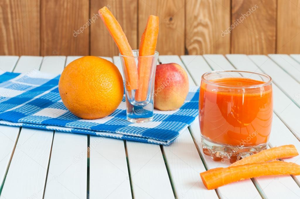 Healthy homemade carrot juice in glass and fresh carrot, apple, orange on light wooden background.