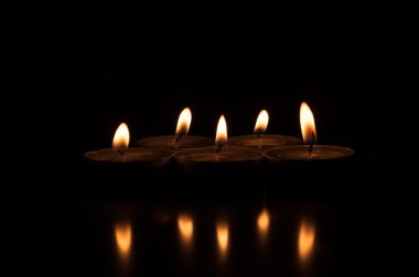 Yüzeyden yansıyan karanlık bir arka plan üzerinde beş mum