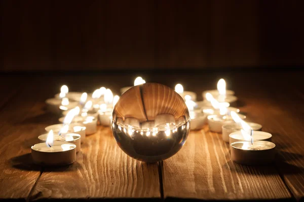 Palla di vetro trasparente e candele accese su vecchio sfondo di legno — Foto Stock