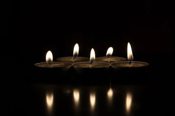 Cinco velas sobre un fondo oscuro reflejadas desde la superficie —  Fotos de Stock