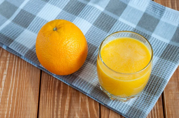 Jugo de naranja casero saludable en vaso y fruta fresca sobre toalla a cuadros gris, fondo de madera . — Foto de Stock