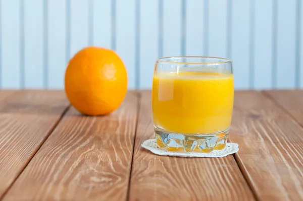 Vaso de zumo de naranja recién prensado con fruta entera sobre mesa de madera — Foto de Stock