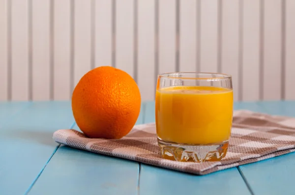 Jugo de naranja casero saludable en vidrio y fruta fresca sobre toalla a cuadros gris, fondo de madera claro . — Foto de Stock