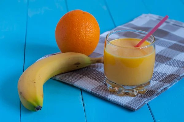 Свежий цитрусовый сок с бананом и апельсином на синем фоне — стоковое фото