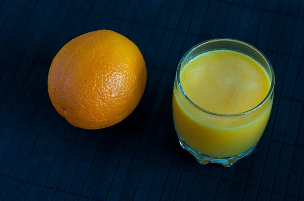 Zumo de naranja en vaso, frutas frescas en un soporte negro de bambú —  Fotos de Stock