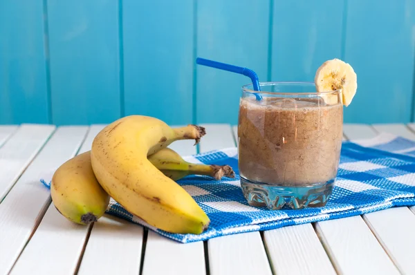 Здоровый домашний банановый сок в стакане и свежие бананы на светлом деревянном фоне . — стоковое фото