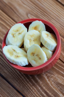 Ahşap doğrama tahtası üzerinde bir seramik kase taze olgun organik dilimlenmiş muz