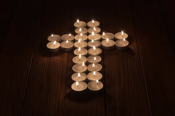 Lit tea lights in the shape of a cross on  wooden surface. — Stock Photo, Image