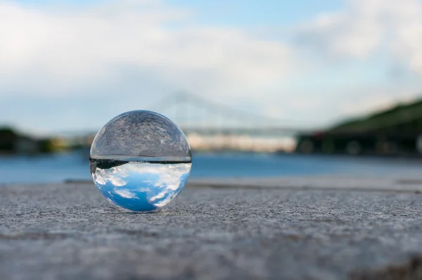 Bola transparente de vidrio sobre fondo de puente y superficie granulada. Con espacio vacío —  Fotos de Stock