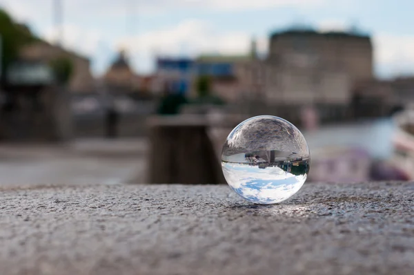 Bola transparente de vidrio sobre fondo de ciudad y superficie granulada. Con espacio vacío — Foto de Stock