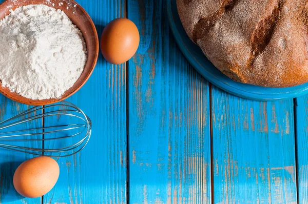 Baking cake in rural kitchen - dough recipe ingredients eggs, flour, butter and whisk on vintage wood table from above. Rustic background with free text space. — Stock Photo, Image
