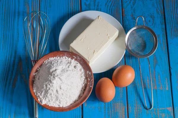 Baking cake in rural kitchen - dough recipe ingredients eggs, flour, butter and whisk, screen on vintage wood table from above — Stock Photo, Image