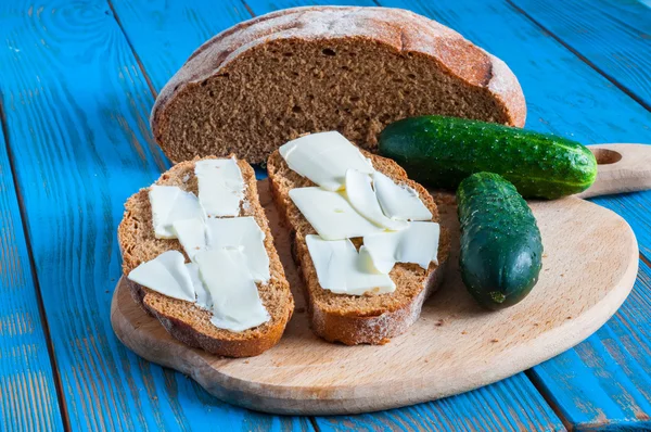 Φρεσκοψημένο ψωμί, αγγούρι και το βούτυρο όλα για σάντουιτς σε αγροτικές ή ρουστίκ κουζίνα σε εκλεκτής ποιότητας ξύλινος πίνακας από ψηλά. — Φωτογραφία Αρχείου