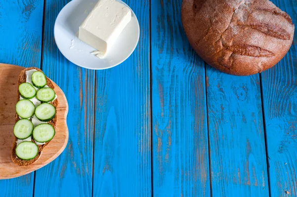 Φρεσκοψημένο ψωμί, σάντουιτς με φέτες αγγούρι και το βούτυρο στο πιάτο στην αγροτική ή ρουστίκ κουζίνα στο εκλεκτής ποιότητας ξύλινος πίνακας από πάνω. Κενό χώρο για κείμενο — Φωτογραφία Αρχείου